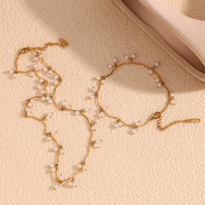 18K gold plated stainless steel pearl necklace and bracelet set on a beige textured surface