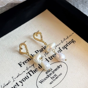 Detailed view of baroque pearl earrings with textured gold heart studs on vintage box