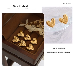 Detail of gold heart earrings with hammered texture displayed in a wooden jewelry box