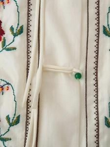 Détail de broderie florale sur un gilet blanc avec boutons de perles vertes traditionnels