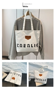 Detail view of large white canvas tote bag with brown leather logo patch and black print