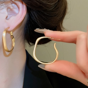Close-up of irregular matte gold hoop earrings with silver pins worn by a model