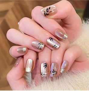 Close-up of champagne gold press on nails with elegant black leaf patterns and glitter