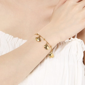 Detailed view of a gold shell pendant bracelet worn on a wrist for a tropical summer look