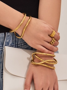 Dettaglio di bracciale rigido a C dorato irregolare con anelli a cuore sovrapposti