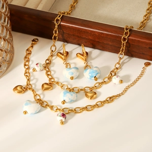 Détail d'une parure dorée avec des charms en forme de cœur bleu et blanc et motifs floraux