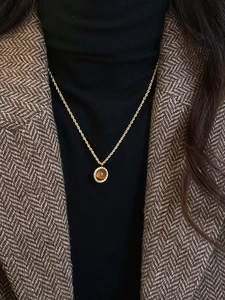 Détail du collier pendentif œil de tigre rond sur chaîne dorée porté sur un blazer