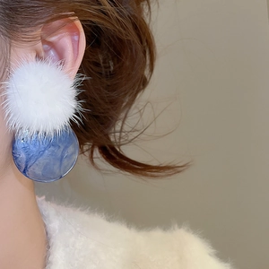 Detail of white fur ball earrings with blue marble round pendants worn by a model