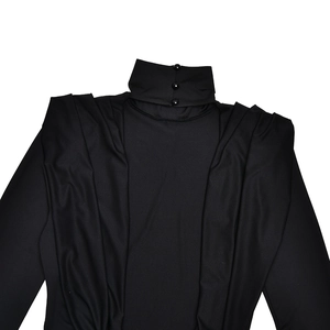 Dettaglio di un top nero a maniche lunghe con collo alto, bottoni e design con pieghe