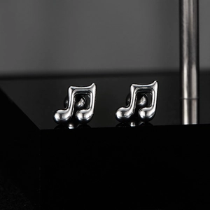 Macro shot of silver eighth note earrings on a sleek black reflective surface