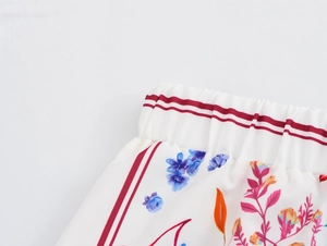 Detail of the elastic waistband with red stripes and vibrant floral print on white fabric