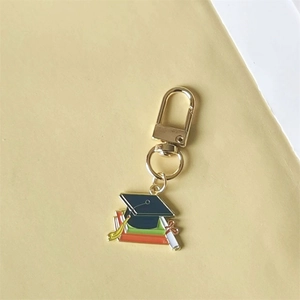Golden graduation cap keychain with stacked books and diploma charm on yellow background