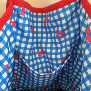 Detailed interior view of tote bag featuring blue gingham lining and red bow patterns