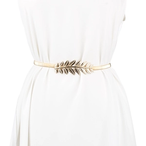 Detail of golden metal leaf buckle on an elastic waist belt over a white dress