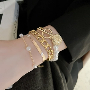 Close-up of four-piece gold bracelet set with OT toggle clasp and coin charm on wrist