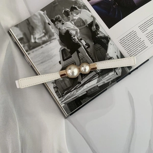 Close-up of elegant thin white leather belt featuring a large double pearl buckle on a magazine