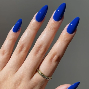 Glossy blue almond fake nails paired with a twisted gold ring on an elegant hand
