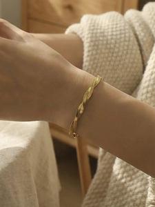 Detail view of a gold twisted cable cuff bracelet worn on a wrist with warm aesthetic tones