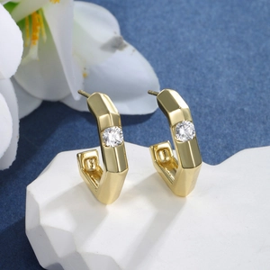 Close-up of geometric C-shaped 14K gold earrings with round zircon on white stone stand