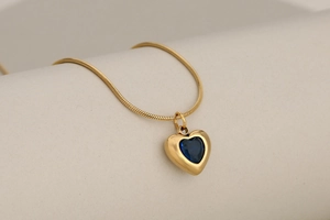 Detailed close-up of golden heart pendant necklace with dark blue crystal on snake chain