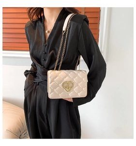 Detailed macro of cream quilted chain bag featuring a gold heart-shaped metal buckle