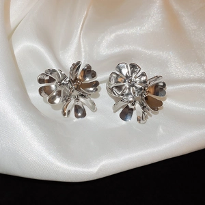 Macro shot of silver floral earrings with polished metal petals on white silk fabric