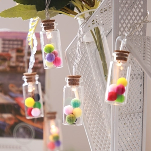 Detail of small glass wishing bottles with colorful pom-poms and warm LED lights