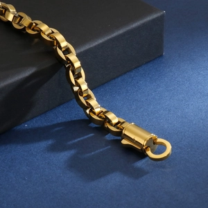 Gros plan d'un bracelet à maillons ovales en acier doré sur un présentoir minimaliste