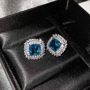 Close-up of square halo earrings with blue center stones and sparkling white diamonds