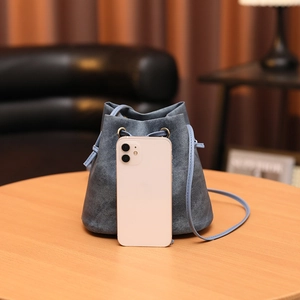 Blue denim drawstring bucket bag with slim shoulder strap on a wooden table display