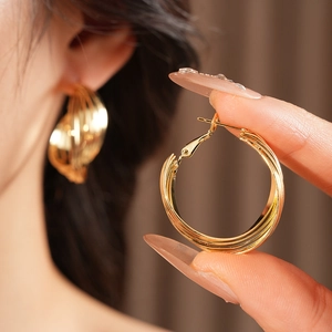 Detail shot of golden multi-layer twisted hoop earrings shown on a model for scale