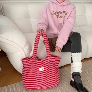 Detail of pink and red striped plush tote bag held by person in pink hoodie