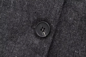 Nahaufnahme von dunkelgrauem Tweed-Stoff mit schwarzem Knopf in Marmor-Optik Detail