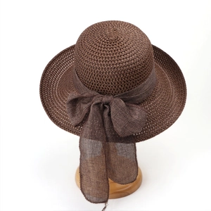 Detail of hollow-weave dark brown straw hat with large flax bow on wooden stand