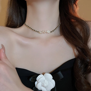 Close-up of woven gold chain and black leather choker with camellia flower and crystals