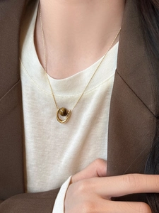 Close-up of a U-shaped gold necklace with a brown tiger eye stone on a model in a blazer