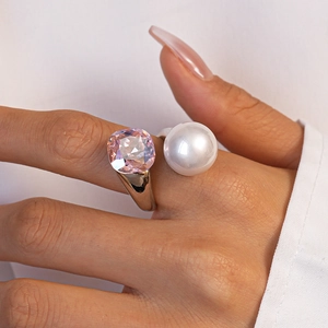 Close-up of pink square gem and white pearl on a stylish gold ring worn on a finger