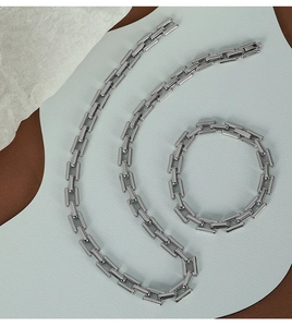 Macro view of minimalist silver chain necklace and bracelet set on textured background