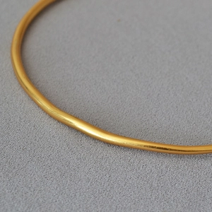 Minimalist gold brass choker necklace with irregular lines on grey fabric background