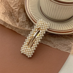 Detail of vintage rectangular pearl hair clip on gold base with textured background