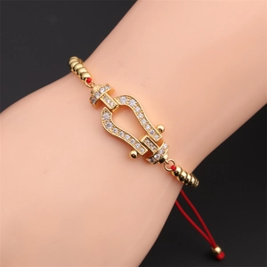 Detailed view of red rope bracelet with gold beads and horseshoe buckle on wrist