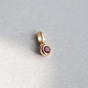 Macro shot of a round gold pendant featuring a faceted red zircon gemstone on marble