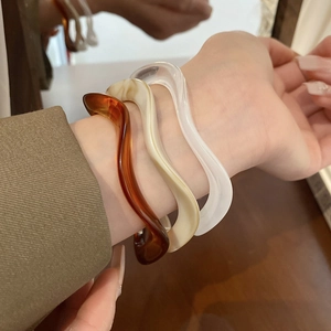 Close-up of wavy resin bangles in amber, cream, and clear colors with a polished finish