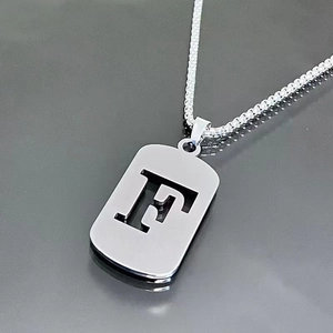 Vue macro du collier en titane argenté avec un pendentif ajouré de la lettre F