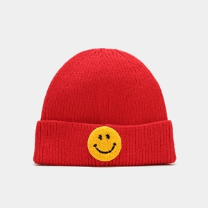 Détail du bonnet en maille rouge avec écusson smiley jaune brodé sur le large revers