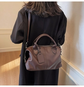 Detail of a dark brown pebble leather Boston bag with reinforced handles and long strap