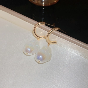 Dettaglio dell'orecchino dorato con perla irregolare su elegante sfondo di seta beige