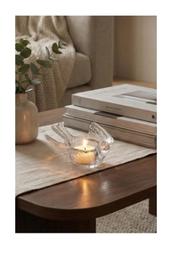 Bird-shaped glass candle holder with tea light on linen runner in cozy home setting