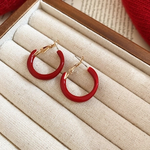 Detailed view of glossy red hoop earrings with gold accents in a beige velvet jewelry box