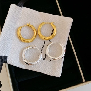 Detail of gold and silver pleated geometric hoop earrings on a white pouch in a black box
